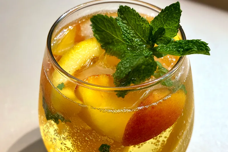 A vibrant pitcher of Refreshing Peach Lemonade Bliss filled with ice and garnished with mint.