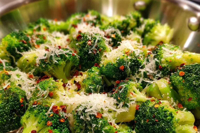 A vibrant display of fresh broccoli, garlic, and parmesan on a wooden cutting board.